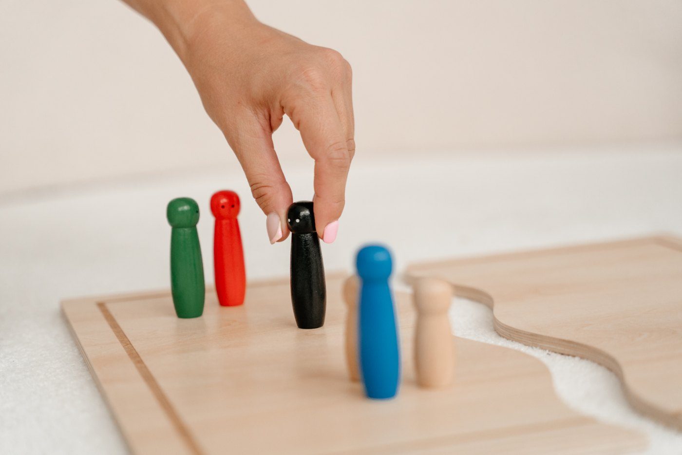 Eine Hand stellt eine schwarze Holzfigur zwischen weitere farbige Figuren auf einem Systembrett