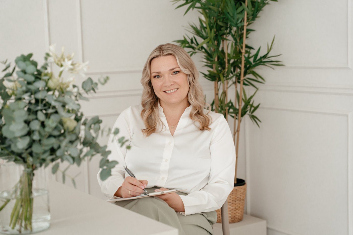Mandy Jäger sitzt in einem hellen Praxisraum mit Bambuspflanze und macht Notizen auf einem Klemmbrett