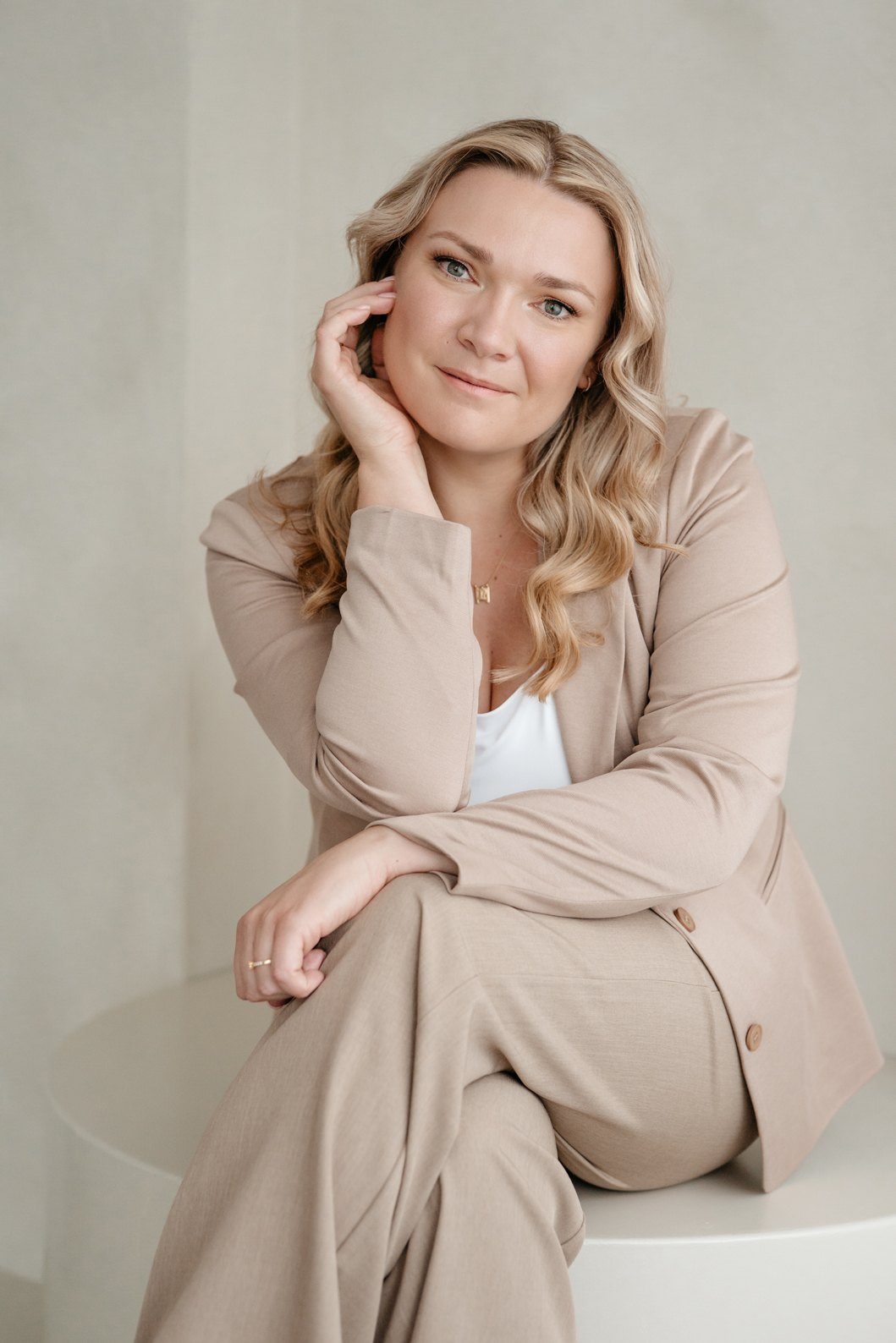 Mandy Jäger sitzt in einem beigen Anzug vor einer hellen Wand und blickt in die Kamera