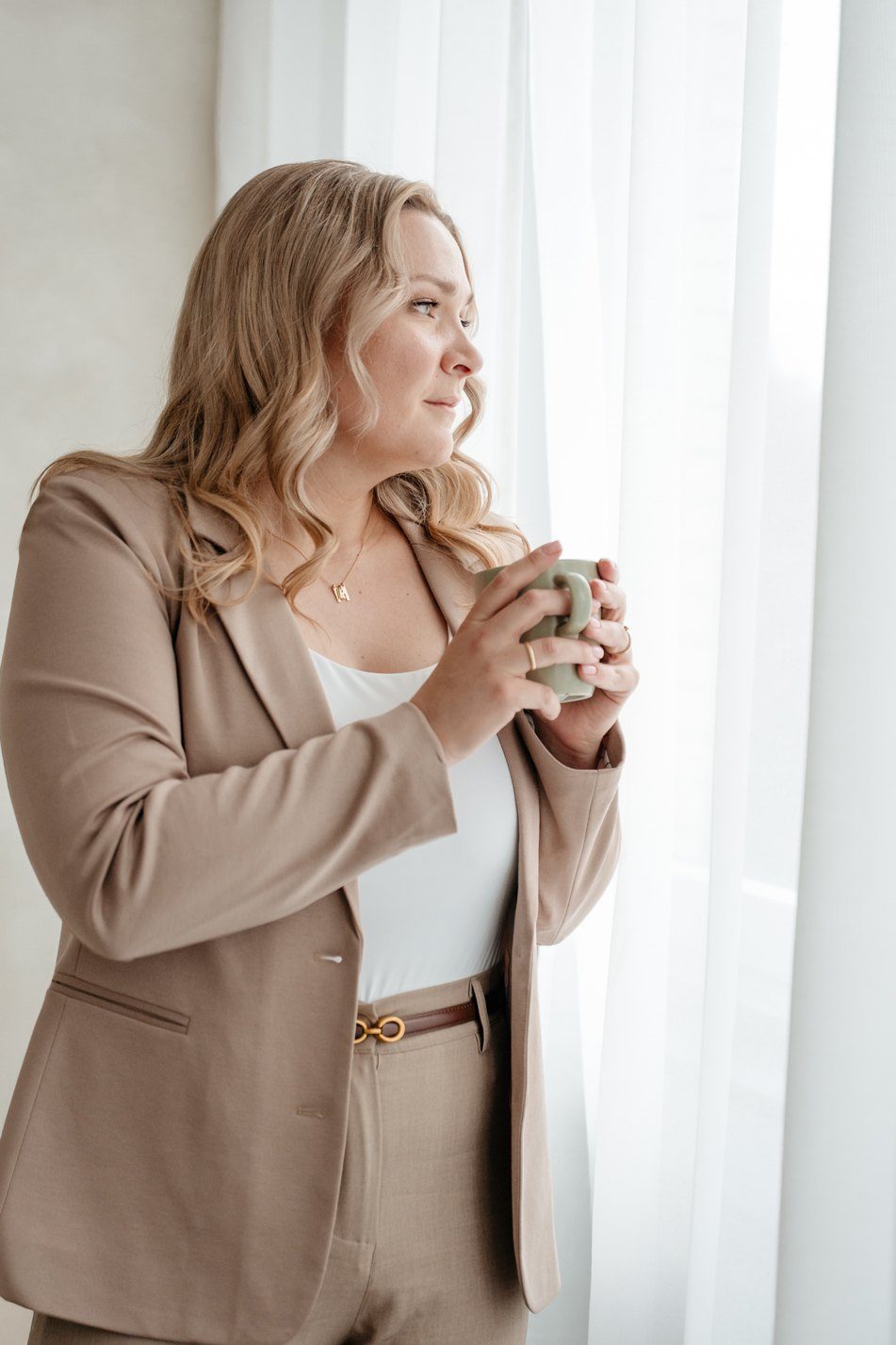 Mandy Jäger steht mit einer Tasse in den Händen am Fenster und blickt nach draußen