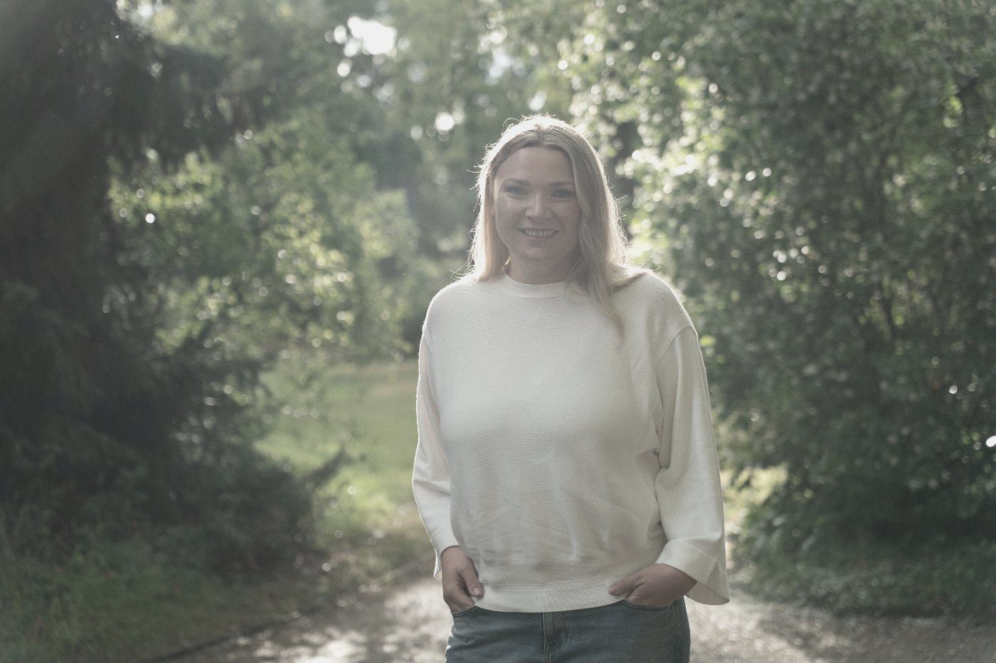 Mandy Jäger steht lächelnd auf einem Weg zwischen Bäumen im Gegenlicht